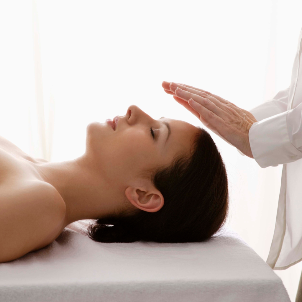 A Reiki practitioner hovers hands above a woman, channeling calming energy.